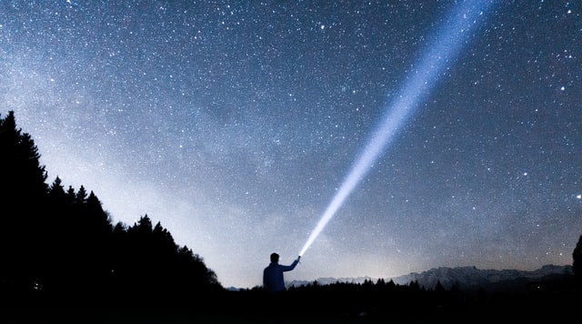 Mann mit Taschenlampe vor Nachthimmel